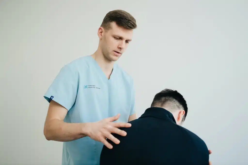 Healthcare professional in medical scrubs performing specialized physical therapy examination, demonstrating professional treatment techniques for scrotal pain relief in a clinical setting with neutral background.